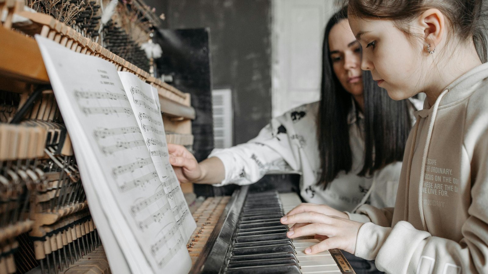 pexels-photo-7521204-7521204 A child learning to play piano with guidance from an adult in a cozy setting, focusing on music sheets.